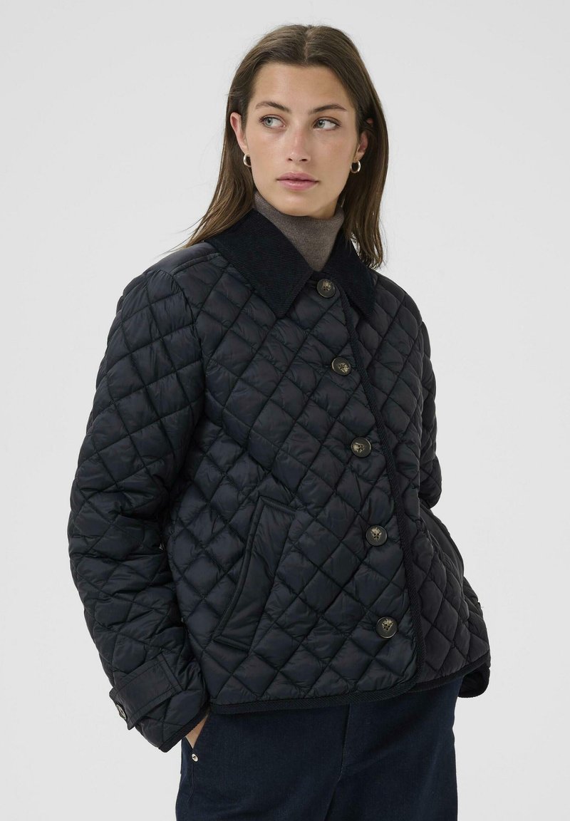 Gequilted zwarte jack met een corduroy kraag, knoopsluiting aan de voorkant en zijzakken. De stof heeft een gladde textuur en een ruitenpatroon.