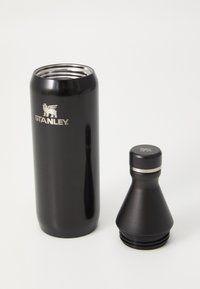 Bouteille d'eau en acier inoxydable noir avec un fond effilé, dotée d'un bouchon à vis et du logo "STANLEY" en argent.