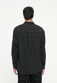 Czarna i szara koszula flanelowa w kratę z kołnierzykiem na guziki, dwoma tylnymi kieszeniami i długimi rękawami. Teksturowany materiał o luźnym kroju.