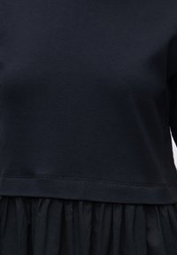 Κοντινό πλάνο ενός ατόμου που φοράει απλό μαύρο τοπ με ορατή ραφή πάνω από μια μαζεμένη μαύρη φούστα ή κάτω μέρος.
