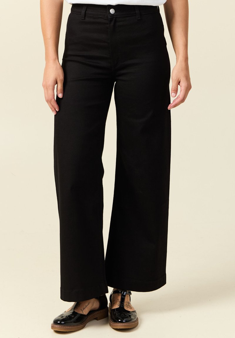 Mustat leveälahkeiset farkut, joissa on korkea vyötärö, etunappi ja siisti helma. Yhdistetty kiiltävän mustiin kenkiin.