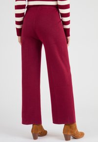 Pantalons à jambes larges en tissu bordeaux profond, avec une texture lisse et une taille élastique. Associés à des bottines à talons beiges.
