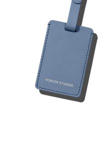 Blue leather luggage tag with a stitched edge and a loop for attachment. Features embossed text: "HORIZN STUDIOS." Smooth texture.
