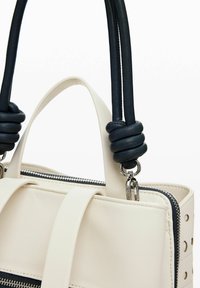 Bolso de mano de cuero blanco con textura suave, con asas en color marino, herrajes plateados y recortes decorativos a lo largo de los lados.