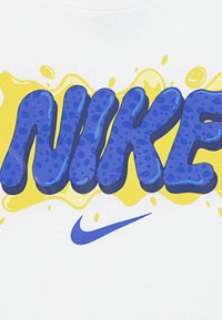 Weißes Kurzarmhemd mit großen, abgerundeten blauen Buchstaben "NIKE" in gepunktetem Muster, akzentuiert durch ein gelbes Spritzdesign.