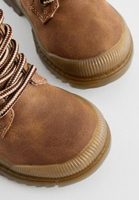 Bottines en faux cuir marron avec une finition texturée, bout rond et lacets contrastés beige et bourgogne. Semelles en caoutchouc épaisses avec des rainures.