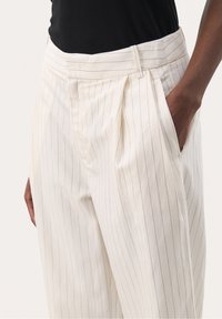 Pantalon blanc à fines rayures avec devant plissé, poches latérales et ceinture structurée. Le matériau semble léger et lisse.