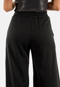 Pantalones de pierna ancha negros hechos de una tela suave y lisa. Cuenta con una cinturilla elástica para mayor comodidad y un ajuste holgado en la zona de las piernas.