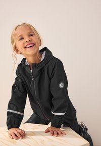 Black waterproof jacket with a zip front, reflective stripes on sleeves, and a hood. The material is smooth with a slight sheen.