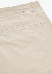 Beige Baumwollhosen mit einer einzelnen Gesäßtasche und einer dezenten gewebten Textur. Etikett auf dem Bund sichtbar.