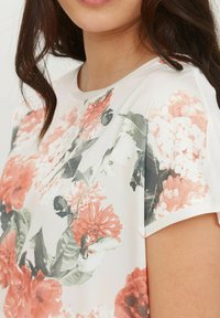 Camiseta floral con escote redondo, mangas cortas, presenta un patrón floral en rosa y blanco, fabricada con tejido suave y de corte relajado.