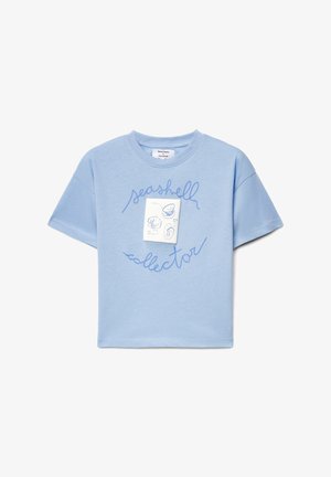 T-shirt di cotone azzurro chiaro con maniche corte e collo rotondo, con la scritta "collezionista di conchiglie" in corsivo blu e un'etichetta bianca.