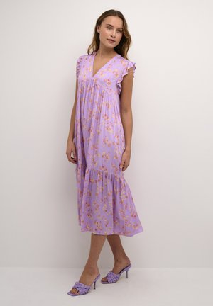 Vestido floral lila con mangas farol con volantes, diseño en capas y escote en V. Combinado con sandalias de tacón lila. Tela suave y ligera.