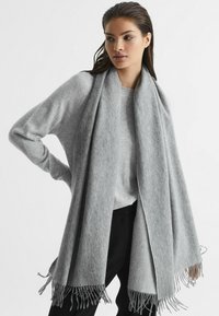 Grå cashmere-blandet tørklæde med frynsede kanter, hængende løst over en lysegrå sweater, der fremhæver den bløde tekstur og drapering.