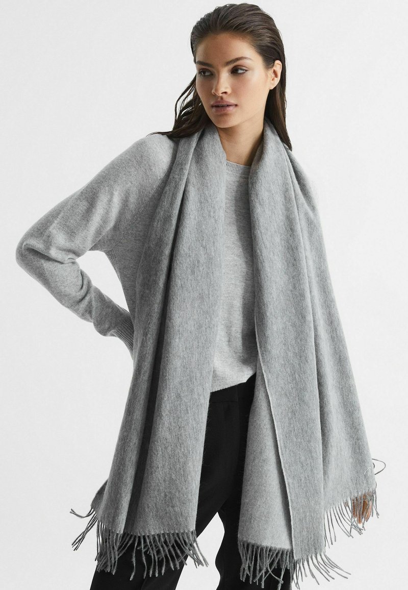 Grå kashmirblandning halsduk med fransade kanter, löst hängande över en ljusgrå tröja, vilket visar på mjuk textur och drape.