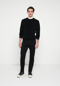 Μαύρο πουλόβερ με υφασμένο σχέδιο, στρογγυλή λαιμόκοψη, ριμπ μανσέτες, συνοδευόμενο από μαύρο παντελόνι στενής γραμμής και ναυτικά αθλητικά παπούτσια με λευκές σόλες.