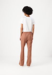 Mønstret brune bukser med røde side-striber, elastisk talje og en afslappet pasform, parret med en ensfarvet hvid t-shirt.