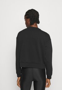 Čierny skrátený sweatshirtn s okrúhlym výstrihom, dlhými rukávmi a rebrovanými manžetami. Hladký materiál s voľným strihom. Viditeľný šev na leme.