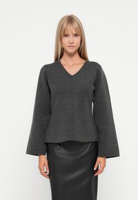 Maglione grigio in lana a v con maniche a campana, caratterizzato da un corpino aderente e un orlo leggermente svasato. Indossato con una gonna di pelle nera.