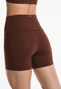 Brown high-waisted shorts made of stretchy fabric. Features a seamless design and a snug fit with a smooth texture. Brand logo visible.