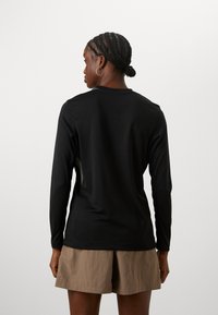 Long-sleeve black top made of smooth fabric, featuring a round neckline and subtle side panels. Paired with beige shorts.