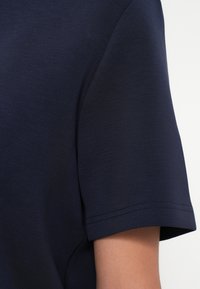 Μπλέ σκούρο κοντομάνικο πουκάμισο σε χέρι ατόμου, δείχνοντάς το υλικό του υφάσματος και την καθαρή ραφή του μανικιού.