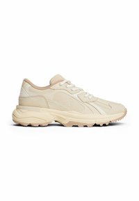Baskets de sport beiges en cuir et matériaux synthétiques, avec une semelle en caoutchouc épaisse, un design à lacets et des accents contrastants.