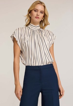 Crème blouse met marineblauwe verticale strepen, hoge halslijn en korte mouwen. Gepaard met op maat gemaakte marineblauwe broeken, met een gladde textuur en subtiele drape.
