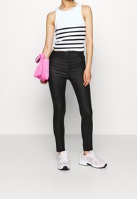 Czarne, dopasowane spodnie o wysokim stanie z zapięciem na guziki, połączone z białym topem na ramiączkach w czarne paski, trzymając różową torebkę.