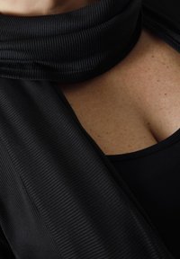 Zwarte geribbelde sjaal met een zachte textuur om de nek gedrapeerd, aangevuld met een zwart bovenstuk. Close-up weergave die de stofdetails benadrukt.