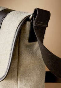 Gray felt bag with dark brown fabric strap, featuring shiny silver hardware and curved edges. Smooth texture with visible stitching detail.