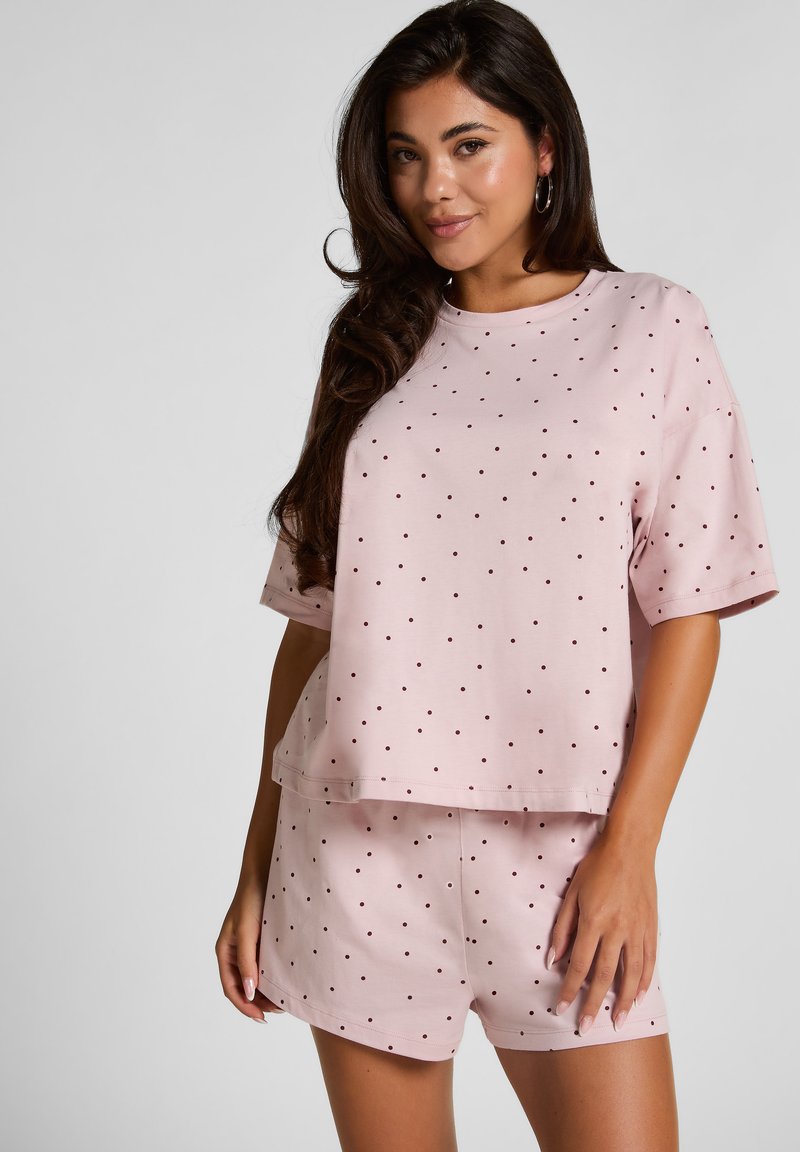 Helles rosa Lounge-Set mit einem Kurzarmoberteil mit dunklen Punkten und passenden Shorts. Weicher Stoff, lockerer Schnitt, minimales Design.