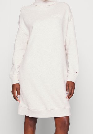 Jasnobeżowa długa sukienka z golfem i długim rękawem, z żebrowanymi mankietami oraz małym logo na piersi i lewym rękawie.