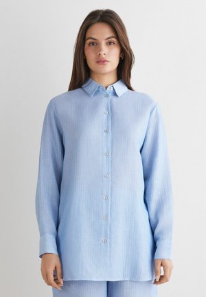 Lichtblauwe, langarmat shirt met een button-down kraag. Heeft verticale strepen, een rechte snit en een voorkant met een stolpelsluiting met zilveren knopen.