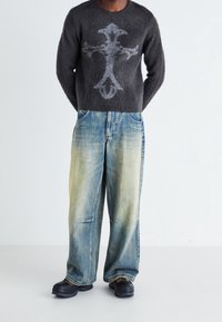 Černý vlněný svetr s šedým křížovým vzorem, kombinovaný se světle modrými širokými denimovými džíny. Celý outfit doplňují černé slip-on boty.