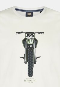 Hvid T-shirt med et centralt grafik af en motocrosscykel i grøn og sort, med detaljeret dækmønster, nummer 89 og logotekst nedenfor.