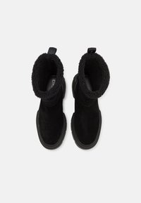 Bottes de cheville en suede noir avec un col texturé et duveteux. Elles présentent un embout arrondi et une épaisse semelle en caoutchouc noir. Design à la fois élégant et pratique.