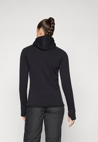 Svart hettegenser med lange ermer, i en tettsittende design, med teksturert stoff og en myk hette. Har tommelhull ved ermene og flatlock-sømmer.