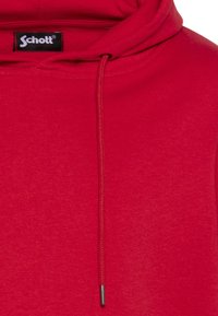 Sudadera con capucha roja hecha de tela suave, con cordón de ajuste con embellecedor metálico y una etiqueta con el logo en el cuello.