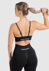 Zwarte sportbeha en high-waisted shorts met wit "SMILODOX" logo. De stof lijkt rekbaar en soepel, wat zorgt voor een aansluitend ontwerp.