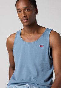 Débardeur en coton bleu clair avec un col rond et un petit logo rouge Levi's brodé sur la poitrine, texture lisse, coupe décontractée.