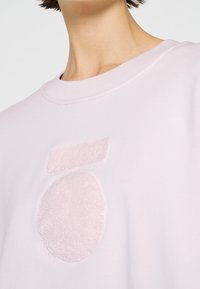Sweat-shirt rose clair avec un motif géométrique duveteux et texturé en rose plus foncé sur le devant, avec un col rond classique.