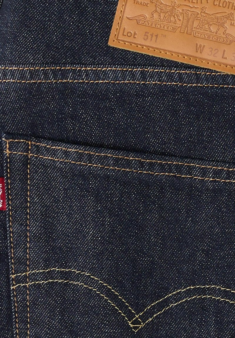 Tasca posteriore di jeans in denim blu scuro con cuciture arancioni, patch in pelle del marchio con scritto Lot 511 e taglia W32 L32, e una piccola etichetta in tessuto rossa.