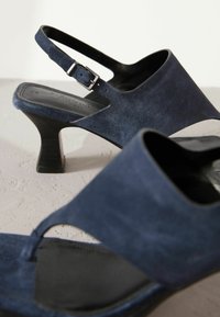 Mørkeblå ruskinds slingback hælesandaler med en lav blokhæl, åben tå, justerbar rem og glat sort indersål.