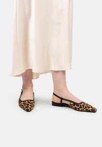 Pantofi cu imprimeu de leopard, cu un design cu vârful ascuțit, margine neagră și bretele la spate. Textură moale, purtați cu o rochie de satin crem.