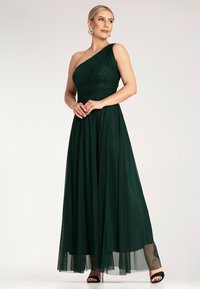 Długa, ciemnozielona sukienka na jedno ramię z lejącego materiału, z dopasowaną górą i marszczonym wzorem, z pełną, kaskadową spódnicą.