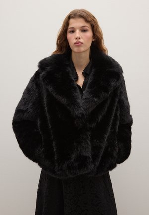 Chaqueta de piel sintética negra con un amplio y esponjoso cuello y un corte holgado. Textura suave y mangas largas, combinada con un vestido negro de encaje.