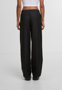 Zwarte wijde broek met een elastische tailleband, gladde stoftextuur en geen zichtbare patronen. De zomen zijn recht en reiken tot de enkels.