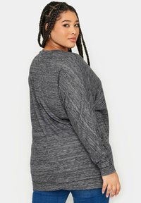Långärmad, melerad grå topp med en avslappnad passform och strukturerad tyg. Har en rundad halsringning och ribbade muddarna. Pairad med blå jeans.