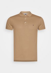 Polo shirt en coton marron avec un col classique, trois boutons, des manches courtes et un petit logo sur la poitrine gauche. Texture lisse.